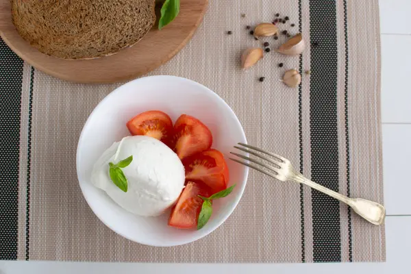 Large mozzarella with slices of tomatoes and basil in a white pl — Stock Photo, Image