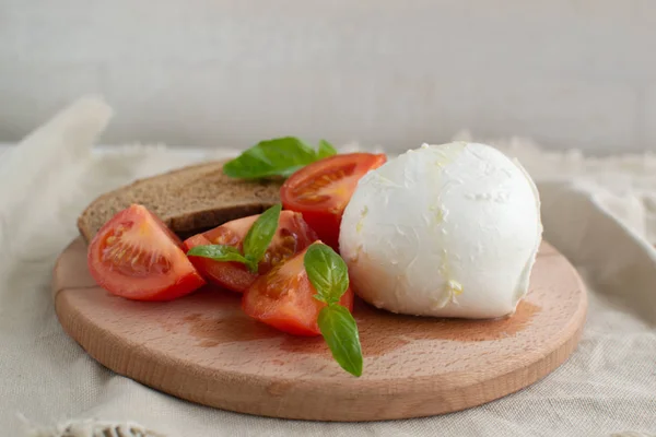 Large mozzarella with slices of tomatoes and basil on a wooden c — Stock Photo, Image