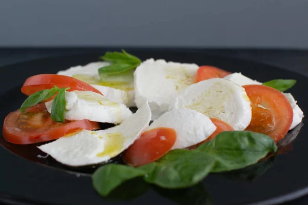 Caprese salad on a large black plate. — Stock Photo, Image