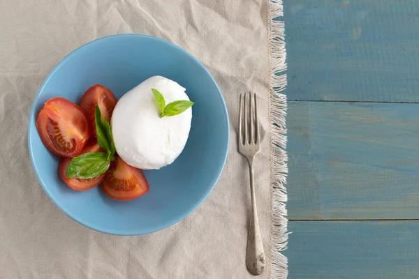 Large mozzarella with slices of tomatoes and basil in a blue pla — Stock Photo, Image