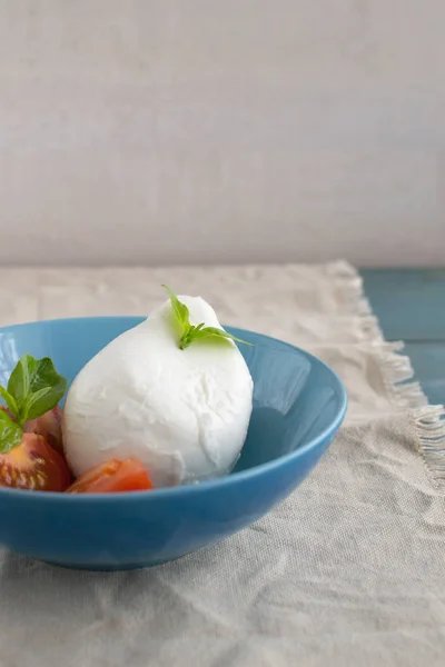 Large mozzarella with slices of tomatoes and basil in a blue pla — Stock Photo, Image