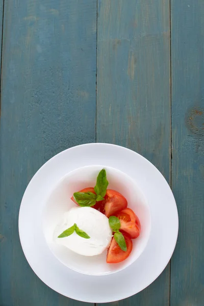 Large mozzarella with slices of tomatoes and basil in a white pl — Stock Photo, Image
