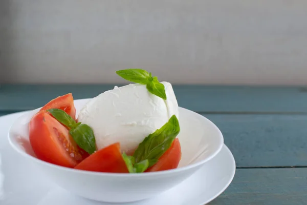 Large mozzarella with slices of tomatoes and basil in a white pl — Stock Photo, Image
