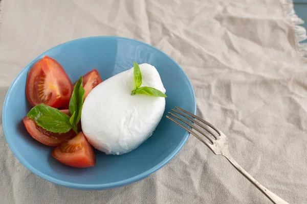 Large mozzarella with slices of tomatoes and basil in a blue pla — Stock Photo, Image