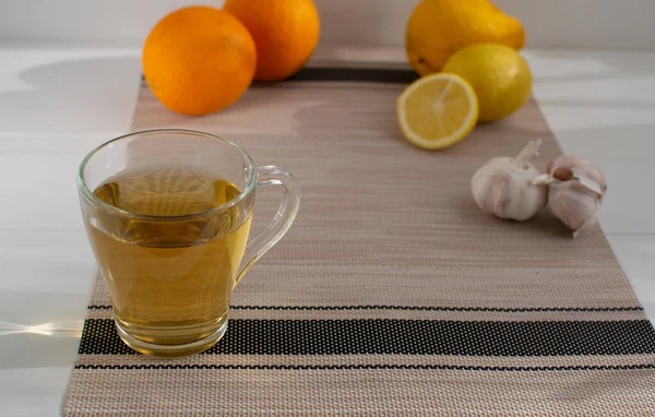 A cup of tea with lemon on a background of oranges and garlic. Set of vitamins becouse of corona virus.