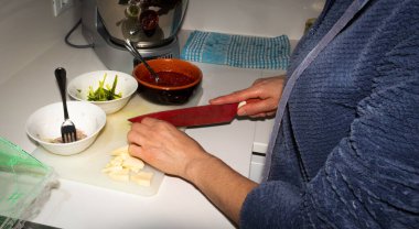 Peyniri bıçakla kesen eller ve domates soslu kuşkonmaz soğanlı pizza hazırlamak için malzemelerle dolu kaseler..