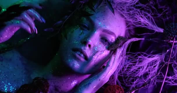 Fantasiewelt. Sexy schöne Mädchen Modell Nymphe liegt in einem mystischen Nebel und blickt in die Kamera Nahaufnahme in Neonlicht mit hellen gesättigten Farben. 4K-Videoqualität — Stockvideo