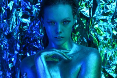 Yaratıcı sanat makyaj. Yüzünde parlak renkli bir boya karışımı olan genç bir mankenin yakın plan stüdyo portresi. Renkli fantezi, sanatsal makyaj. Yan görünüm veya profil, dikey