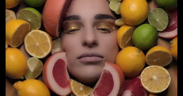Hermosa mujer joven colocada sobre un fondo cítrico junto a rebanadas de limón, que tiene un pedazo de limón en los ojos y sonriente. — Vídeo de stock