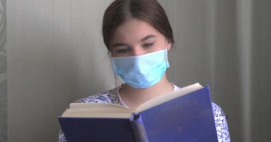 COVID-19 Pandemic Coronavirus genç kadın evde karantina altında maske takıyor ya da Coronavirus hakkında bilgi topluyor. Karantina kızı evde kitap okuyor. Video 4k çözünürlüğü