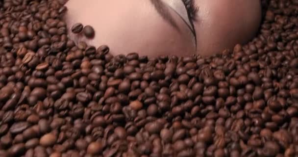 Förälskad i kaffe. Närbild porträtt av vacker ung kvinna med kaffebönor runt henne. Kvinnlig skönhet av hög modell. Titta på kameran. Kaffelivsstil. Hög kvalitet 4k video — Stockvideo