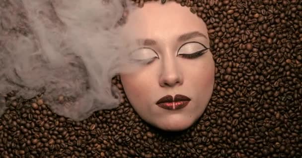 Close up portrait of beautiful young woman with aroma coffee beans around her light steam High fashion model female beauty brown make up. looking at the camera. Coffee lifestyle. High quality 4k video — Stock Video