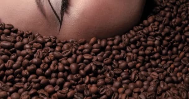 Close up portret pięknej młodej dziewczyny z ziaren kawy wokół niej. Wysoka Modelka Kobieta Piękno Makijaż. Patrzę w kamerę. Styl życia kawy. Wysokiej jakości 4k wideo — Wideo stockowe