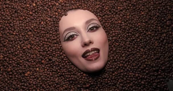 Enamorado del café. Primer plano retrato de una hermosa joven con granos de café a su alrededor. Maquillaje de belleza de mujer modelo de alta moda. mirando a la cámara. Estilo de vida café. Video de alta calidad 4k — Vídeos de Stock