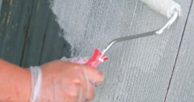 Eldivenli kadın, beyaz renkli, ahşap çitleri yakın plan boyuyor.