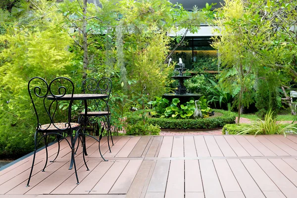 Chaise noire dans patio en bois au jardin vert avec fontaine dans la maison — Photo