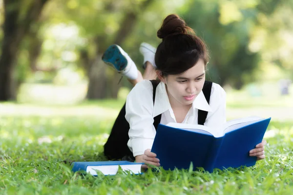 Casual Asya öğrenci kitap okuma çim üzerinde yalan gülümseyerek. Educat — Stok fotoğraf