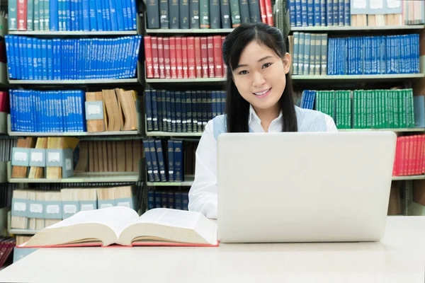 Asiática estudiante con portátil y libros trabajando en la biblioteca en —  Fotos de Stock