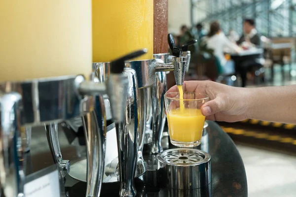 Handen håller glas refill orange juice för rad av färsk juice på — Stockfoto