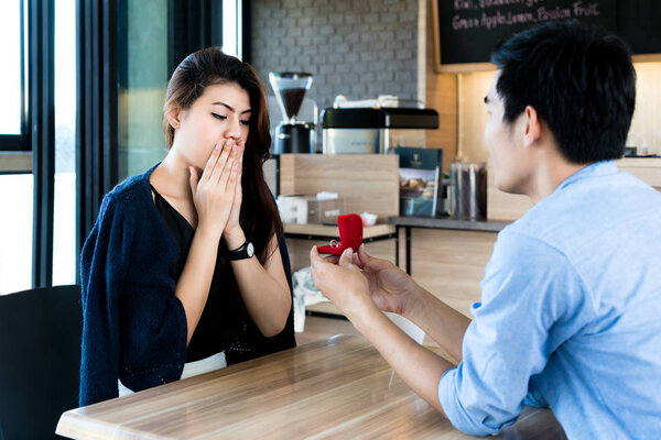 Asian man showing an engagement ring diamond to his amazed girlf