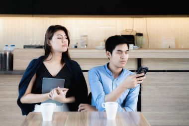 Genç Asyalı aşık çift akıllı telefonlar café'de kullanarak. Kıskanç kız
