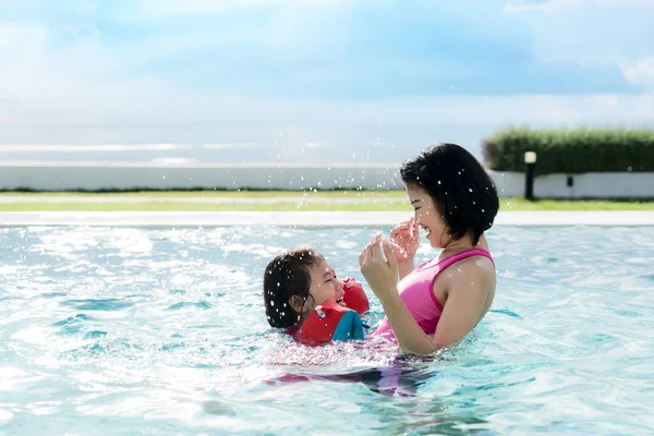 Happy Asian mother and daughter having fun in hotel swimming poo