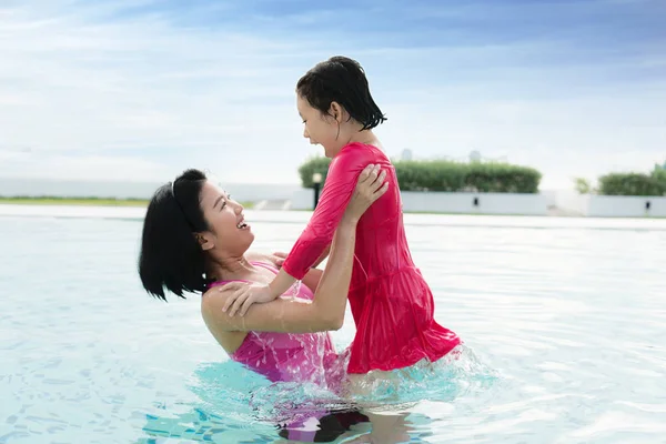 Happy Asian mother raise daughter in hotel swimming pool near se — Stock Photo, Image