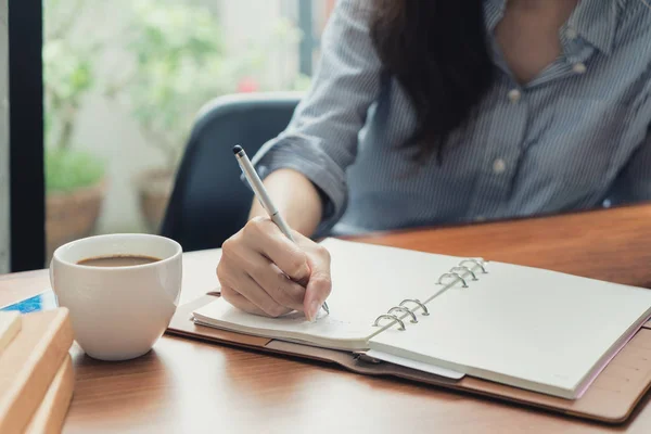 Primo piano di giovane bella donna che scrive nel quaderno mentre si siede — Foto Stock