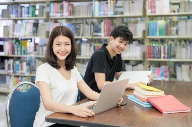 Çift mutlu Asya olan öğrenciler dizüstü bilgisayar ve kitap bahsediyorsun