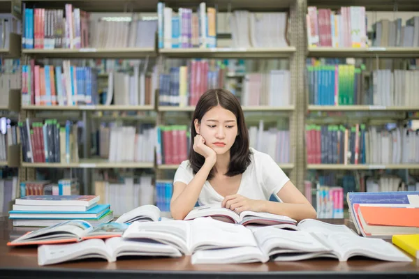 Asiático mulher estudante chato leitura livro na biblioteca com um monte de — Fotografia de Stock