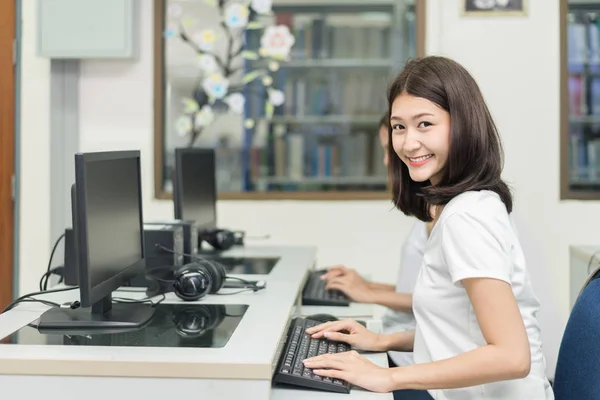 Sonriente mujer asiática estudiante posando con un ordenador mientras studyin —  Fotos de Stock