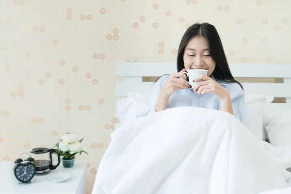 Bedroo でベッドの上に座ってコーヒーを飲みながらアジアの若い女性 — ストック写真