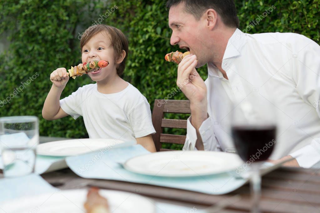Father with little bcute boy eating barbecue in family lunch tim