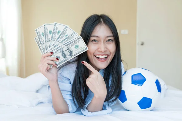 Football and money. Young Asian woman holding soccer ball and ca