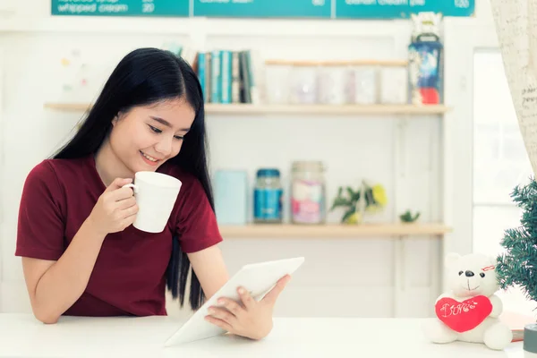 Giovane asiatica sorridente donna sta bevendo caffè in un caffè e holdi — Foto Stock