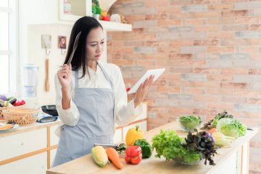 Neşeli Asyalı genç kadın sevinçle mutfakta yemek pişiriyor. S