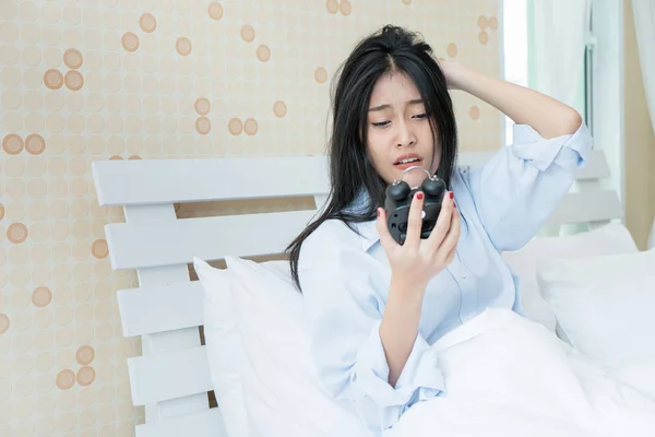 Азиатка держит будильник под одеялом. — стоковое фото