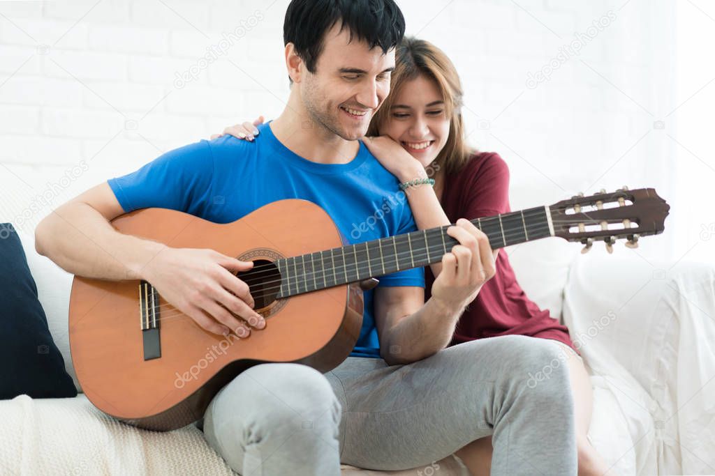 Lover couple young man resting at home and playing guitar for hi