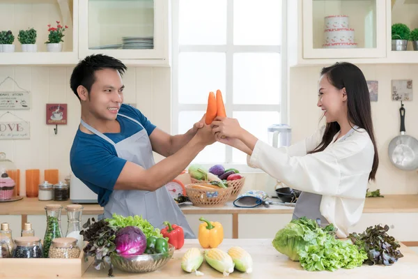 Fun Asian couple mock fighting with carrots as Asian couple cook