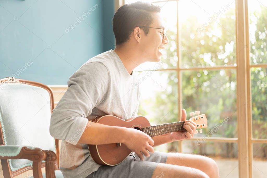 Asian young man hands playing acoustic guitar ukulele at home. E