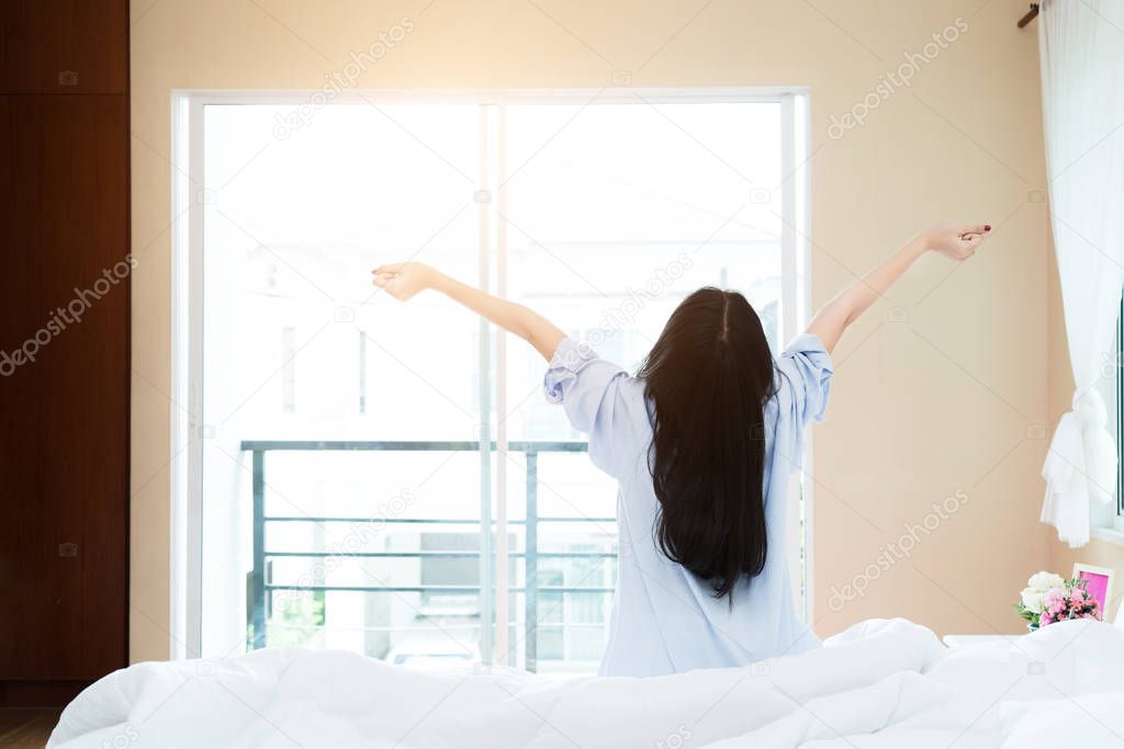 Back view of Asian woman stretching in bed after wake up, rising