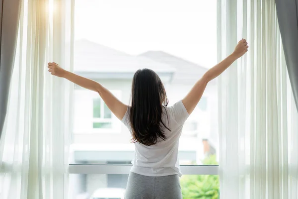 Vista trasera de la mujer asiática estirando las manos y el cuerpo cerca de la ventana a —  Fotos de Stock