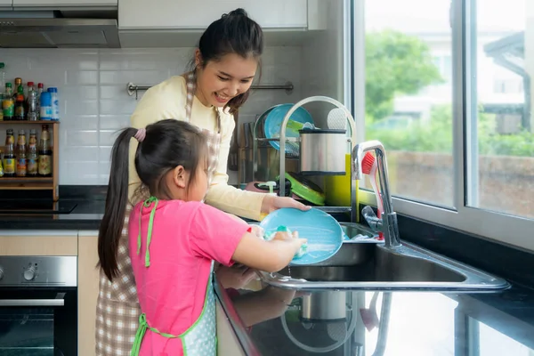 Beautiful Asian mother and daughter having fun while washing dis — Stock Photo, Image