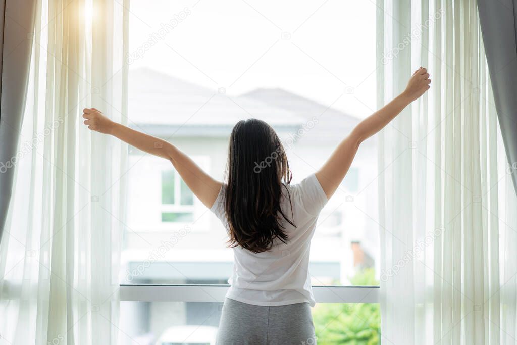 Rear view of Asian Woman stretching hands and body near window a