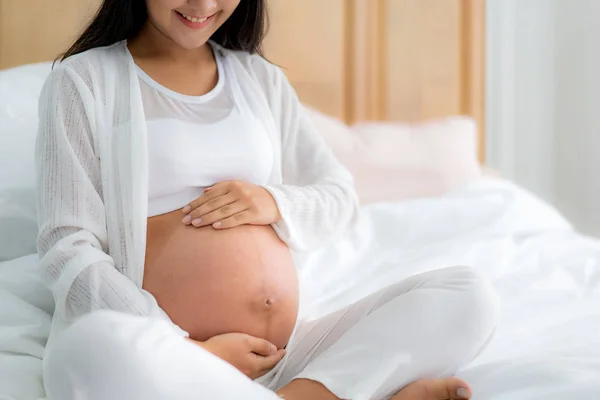 Närbild av glad leende gravid asiatisk kvinna sitter på sängen en — Stockfoto