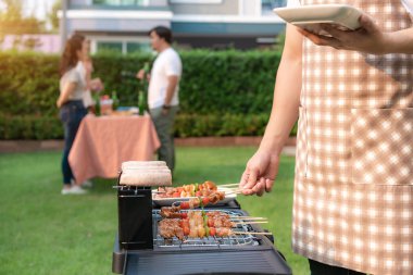 Asian man cooking barbeque grill and sausage for a group of frie