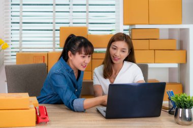 İki Asyalı genç işletme sahibi kadın online alışveriş için masada oturuyor, ofis ekipmanları, girişimci yaşam tarzı konsepti ile teslimat postası siparişlerini kontrol ediyor.