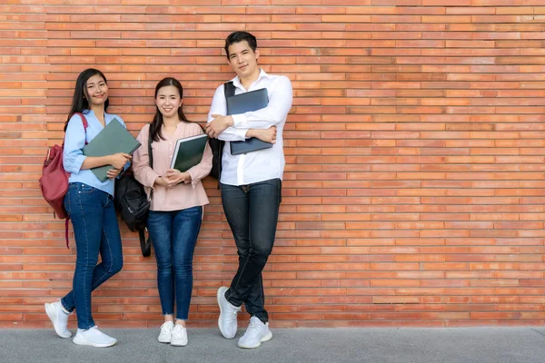 Trzech Azjatyckich Uśmiechniętych Studentów Trzymających Książkę Laptopa Tle Cegły Kampusie — Zdjęcie stockowe