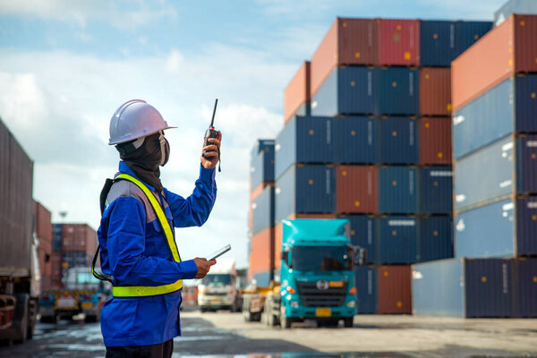 Foreman using and talking walkie talkie to control loading Containers box to truck at Container depot station for Logistic Import Export Background. Business logistic concept