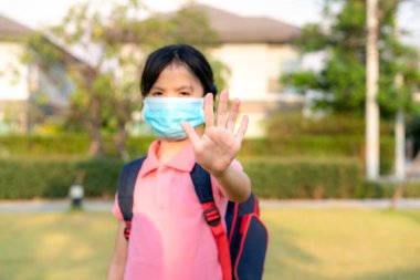 Covid-19 Coronavirus salgını belirtileri ve Hava kirliliği pm2.5 konsepti. Pm2.5 'u korumak için maske takan küçük Asyalı kız Corona virüsünü durdurmak için el hareketi yapıyor.. 